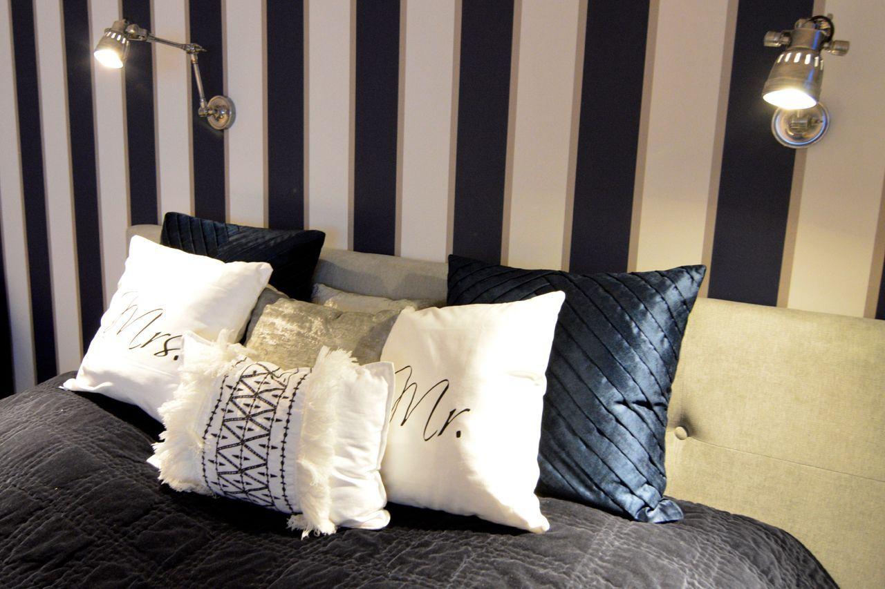 Headboard with pillows and wall lamps against striped wall.