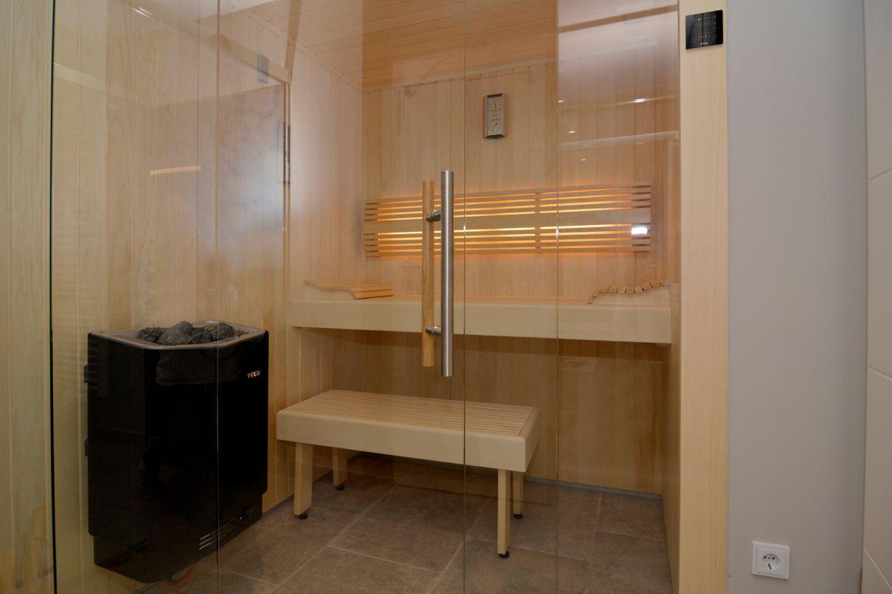 Sauna with wooden bench, glass wall, and heater.