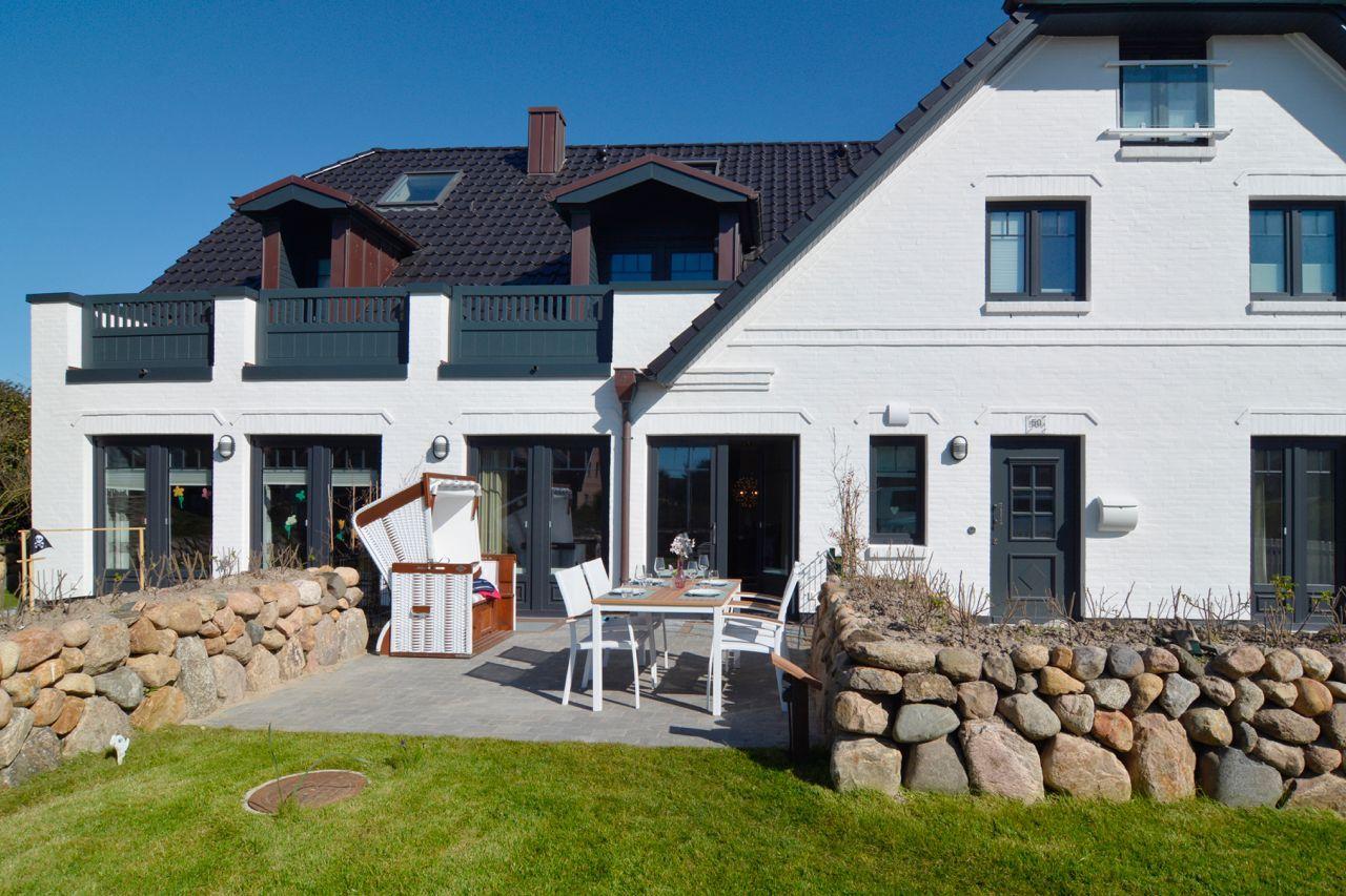White villa with terrace, table and chairs, surrounded by stone walls and grass.