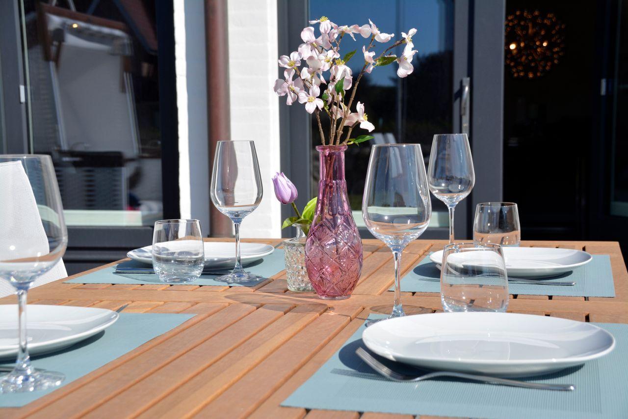 Set table with plates, glasses, and flowers on terrace.