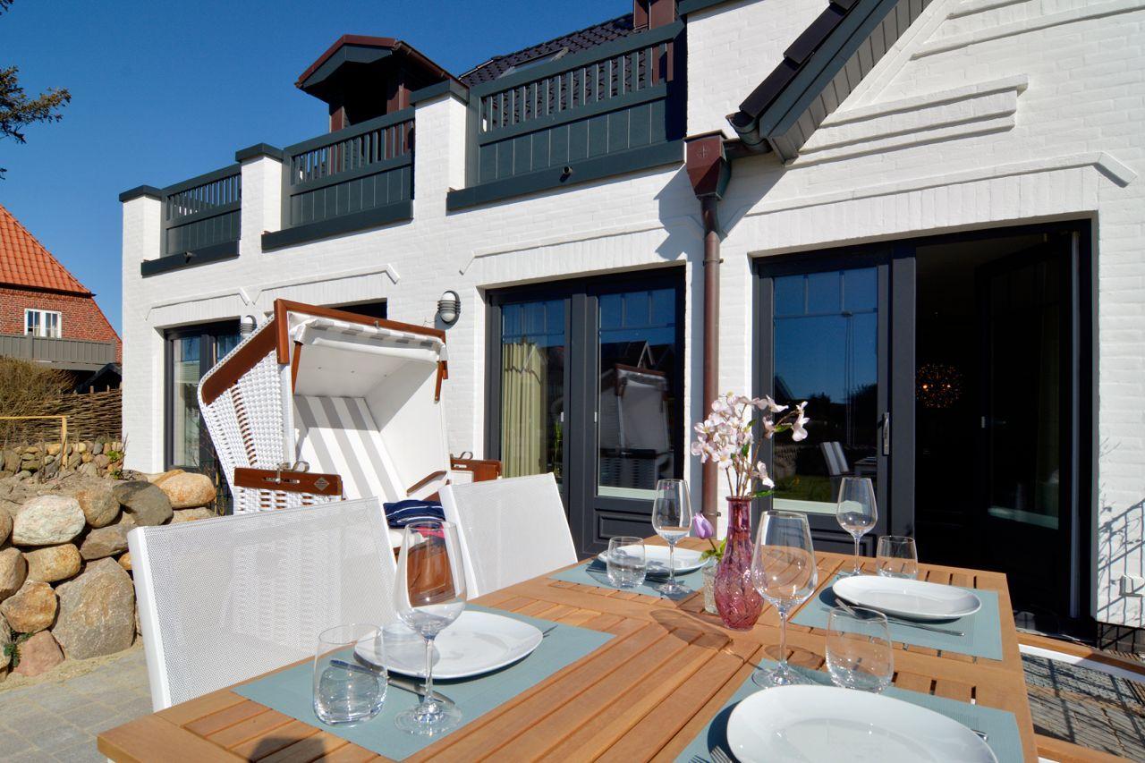 Yellow wooden table with chairs and outdoor table in front of white house with balcony.