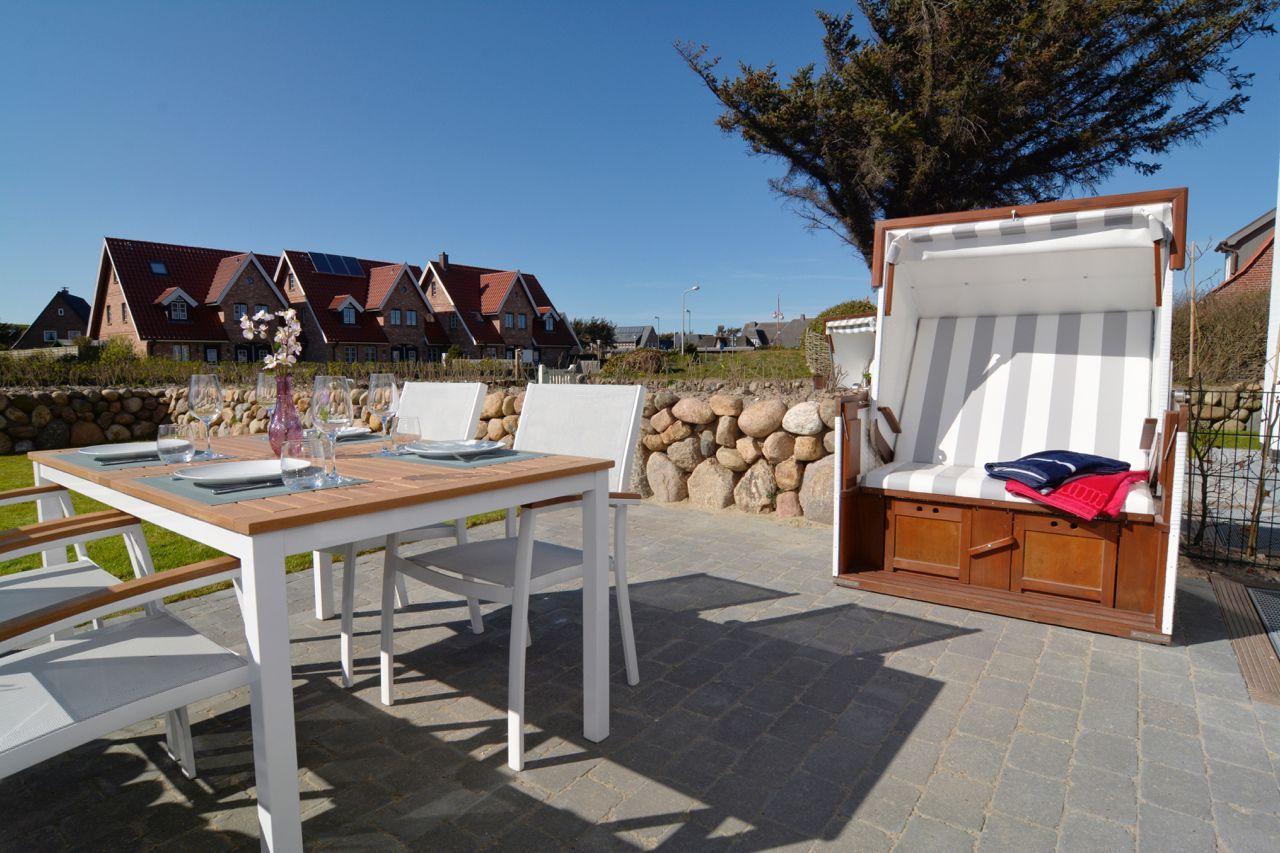 Terrace with dining table, chairs, and beach chair. Houses and stone wall visible in background.