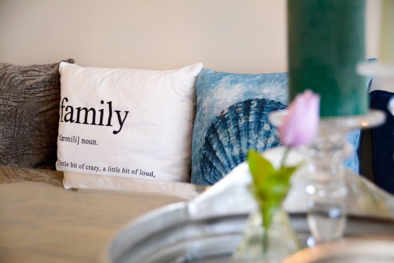 Sofa with cushions, one reading family, beside flower and candle.