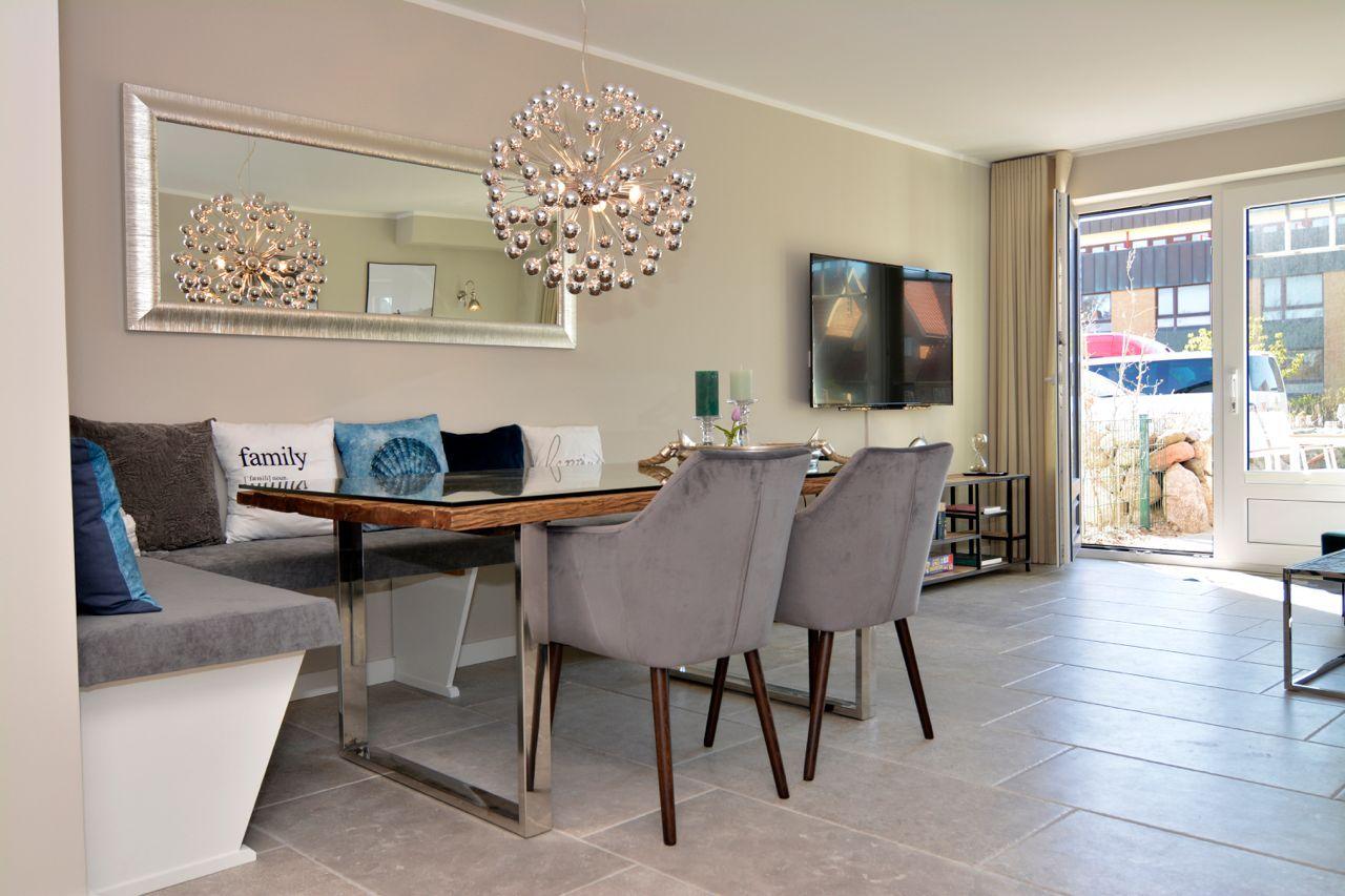 Dining area with glass table, gray chairs, and sofa with cushions. Hanging lamp and mirror on the wall.