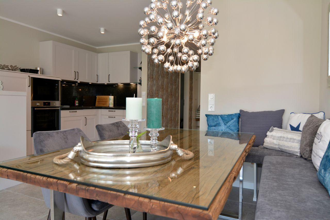 Dining area with glass top and gray corner sofa. Pendant light above table.
