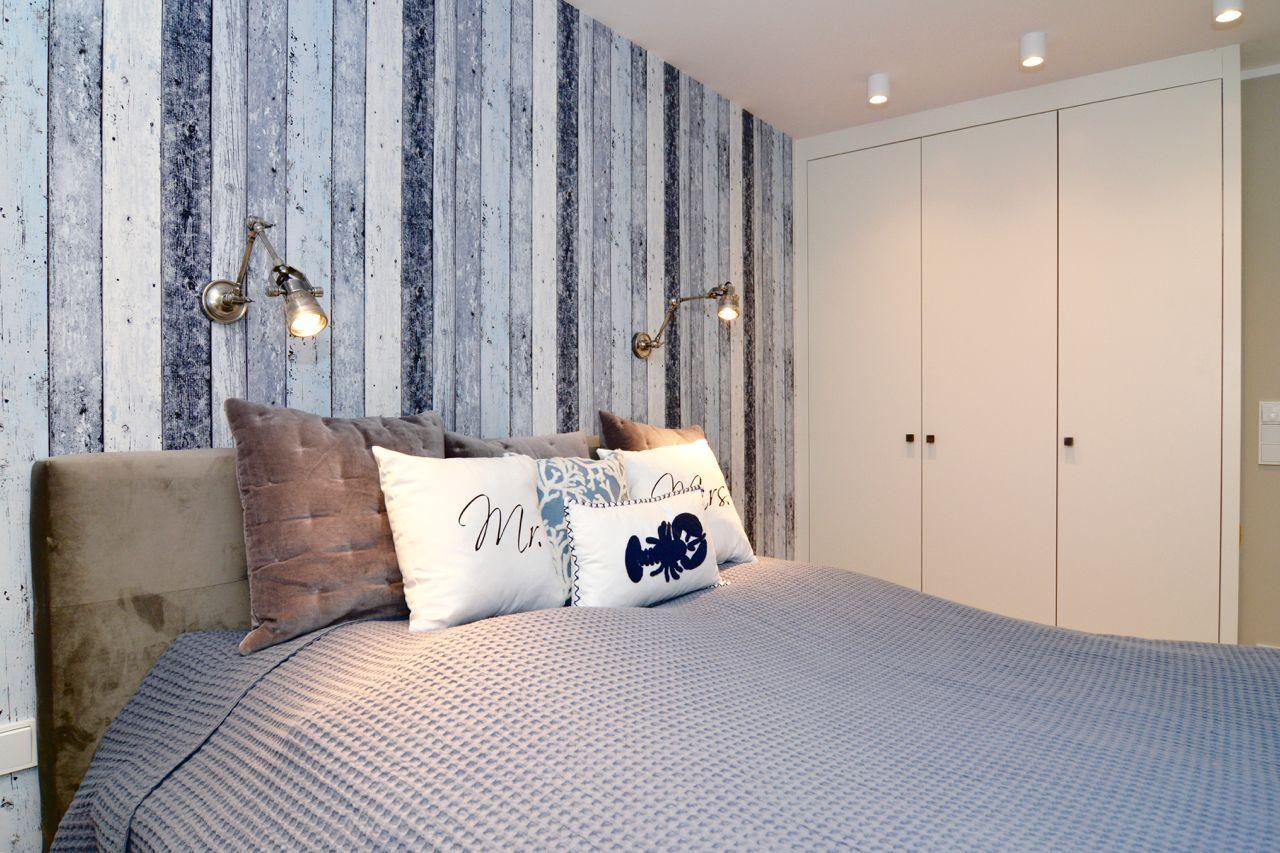 Bedroom with bed, pillows, and wooden wall paneling. White wardrobe and wall lamps.