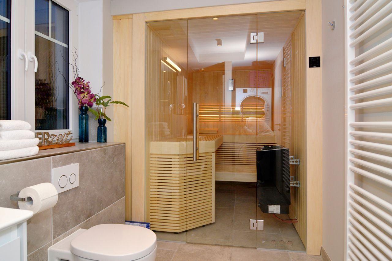 Sauna with glass wall, wooden bench, and heater in bathroom