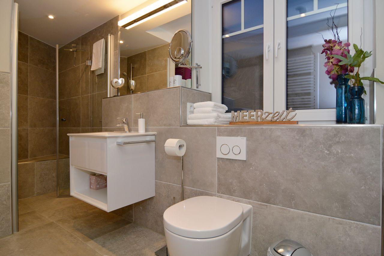 Bathroom with shower, sink and toilet. Window with flowers and towel stack.