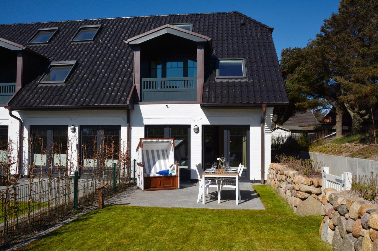House with terrace, garden, and beach chair. Black roof, white walls, and wooden bench.