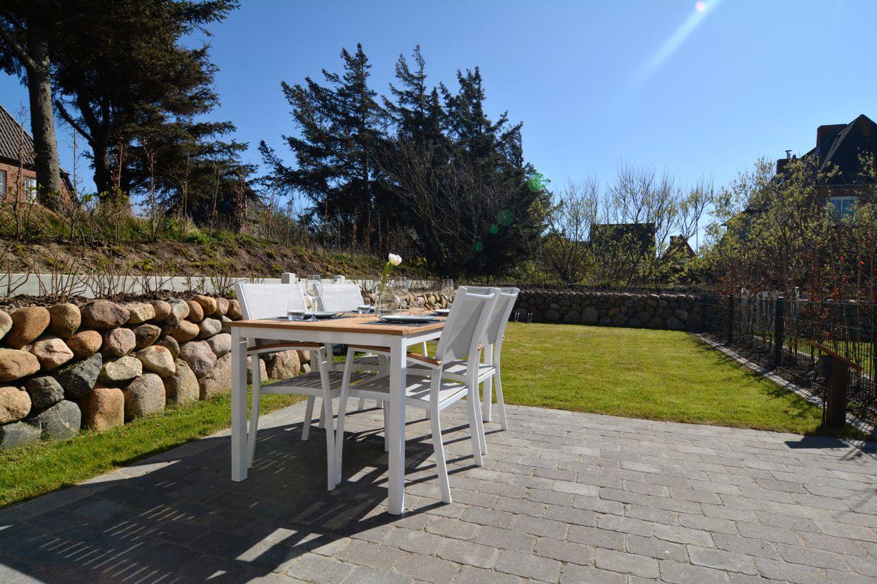 Patio with table and chairs, green lawn and stone wall in background.