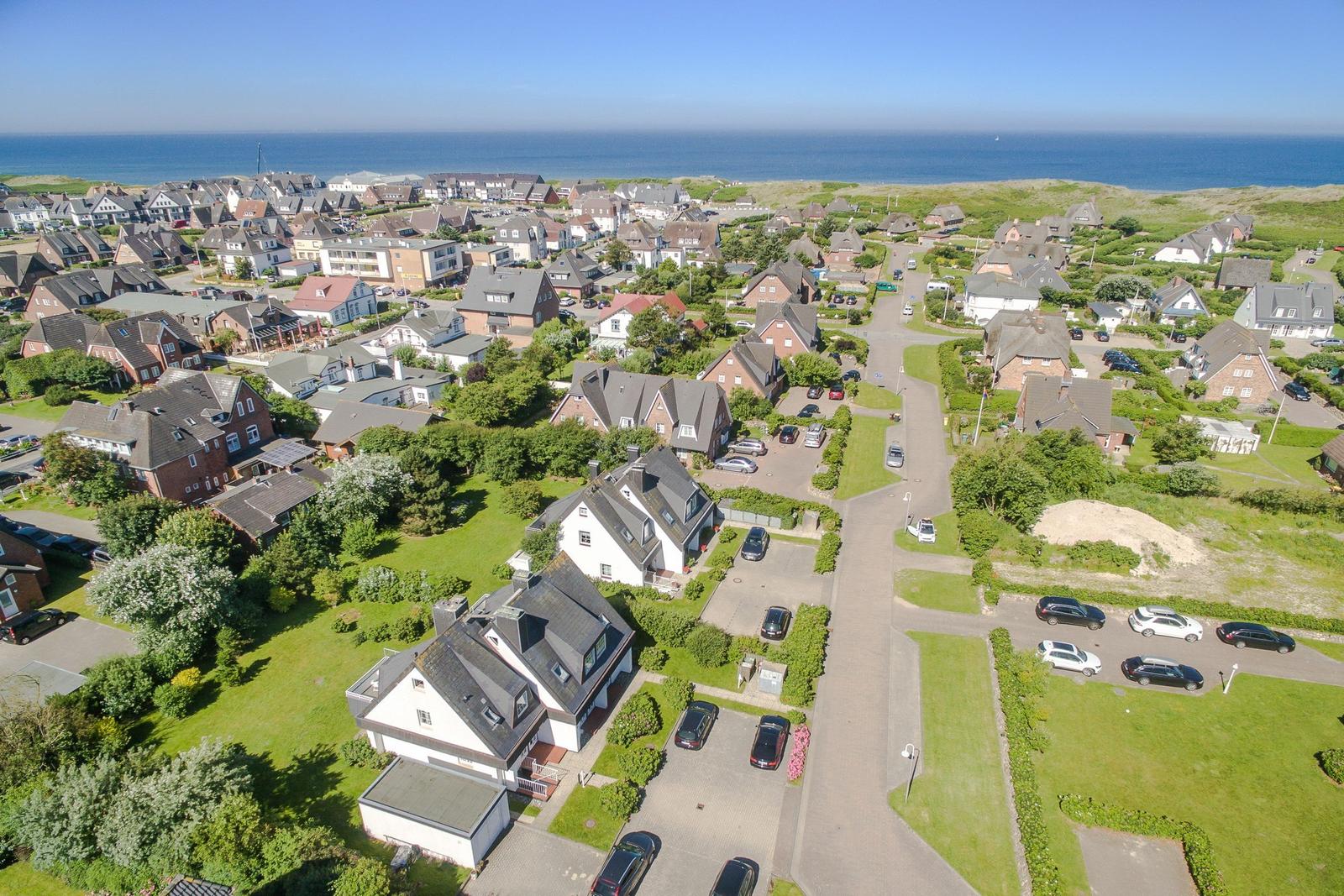 Aerial view of a coastal village with houses, gardens, and the sea in the background.
