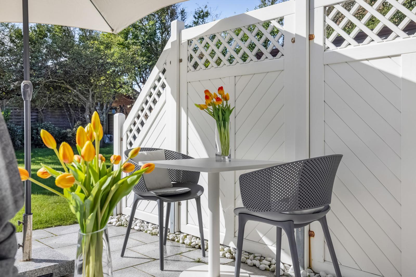 Terrace with table, two chairs, and tulips in vases. White wooden fence and umbrella.