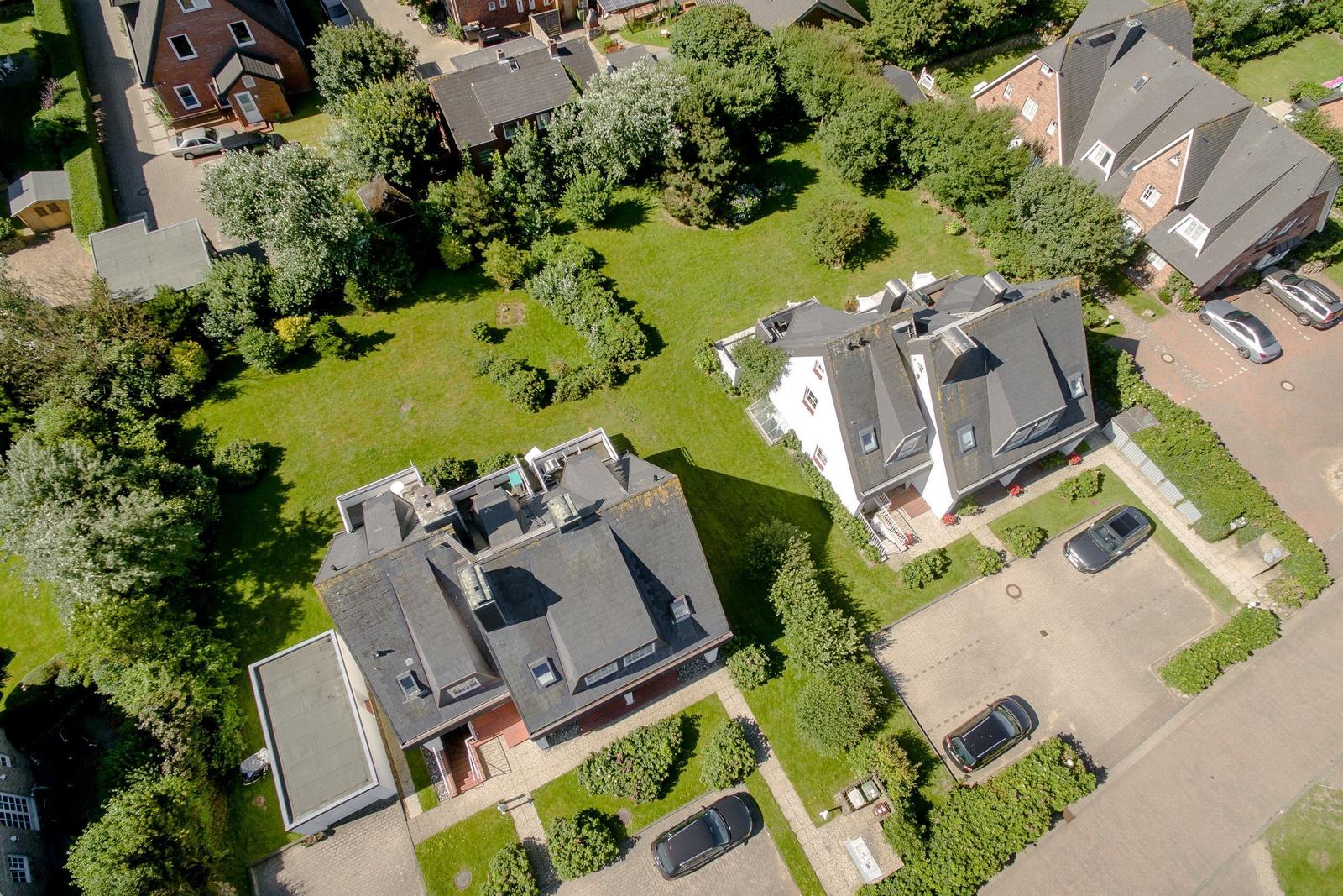 Aerial view of several houses with green lawns and parked cars.