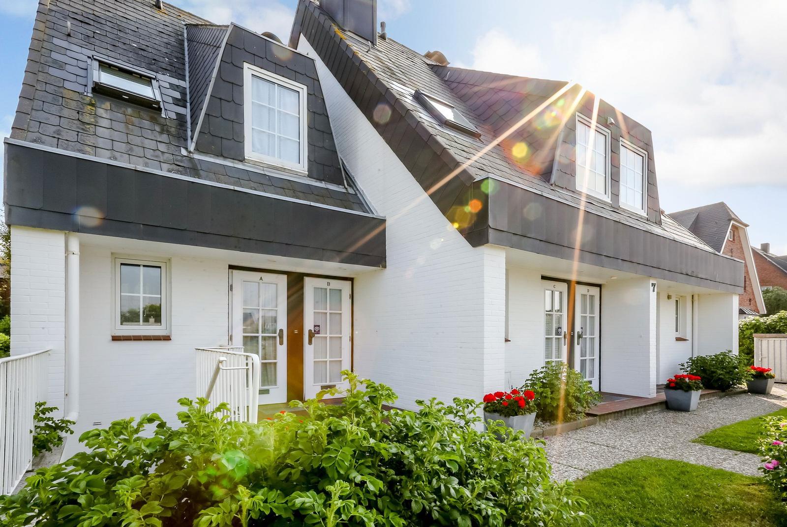 Modern house with white walls and black roof, multiple windows and garden terrace.