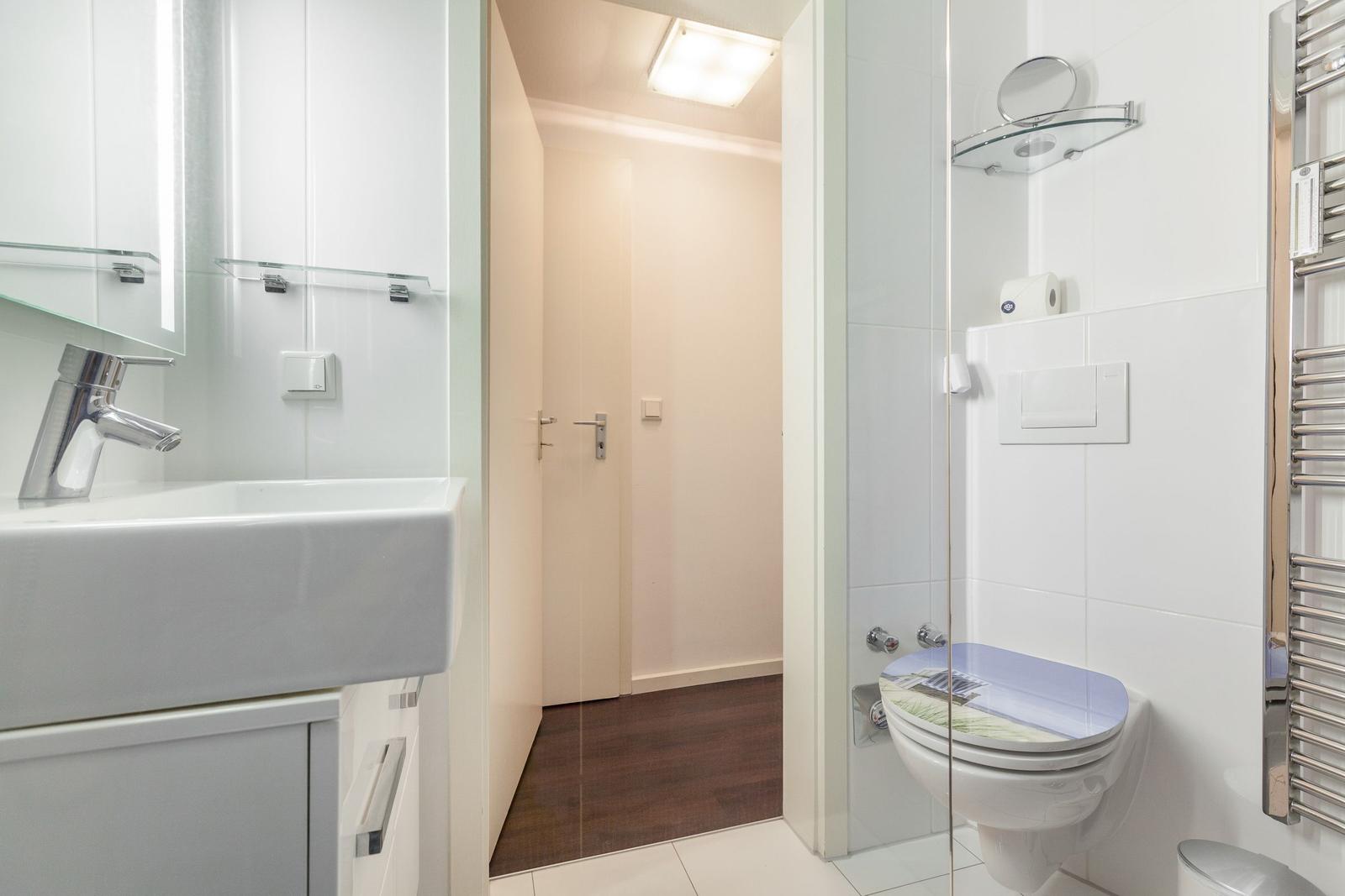 Bathroom with sink, toilet, and shower. Tiled wall and mirror visible.