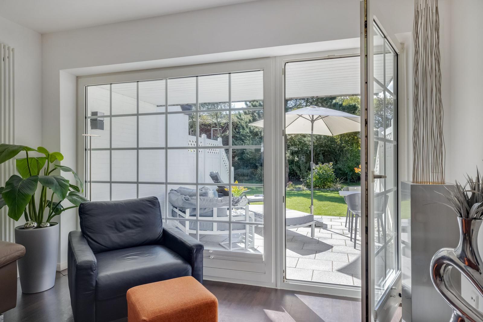 A black armchair and an orange ottoman are in front of a glass door leading to the garden.