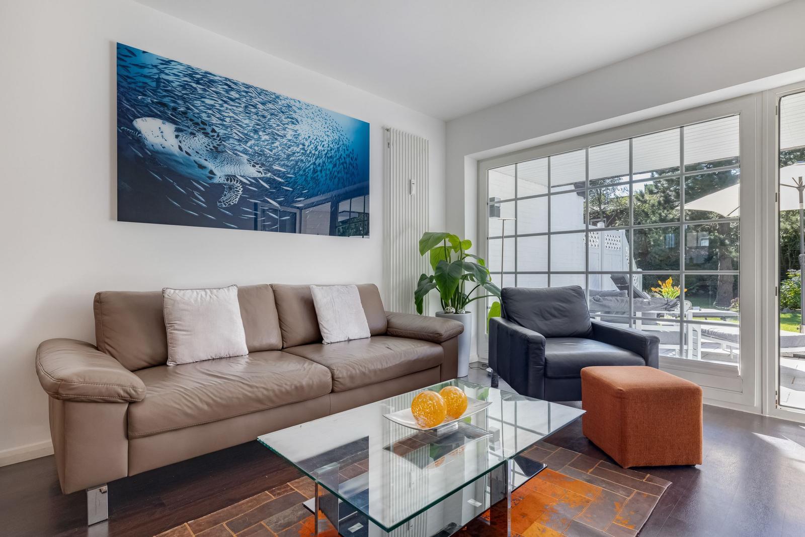Living room with sofa, armchair, and glass table. Large window view to terrace.