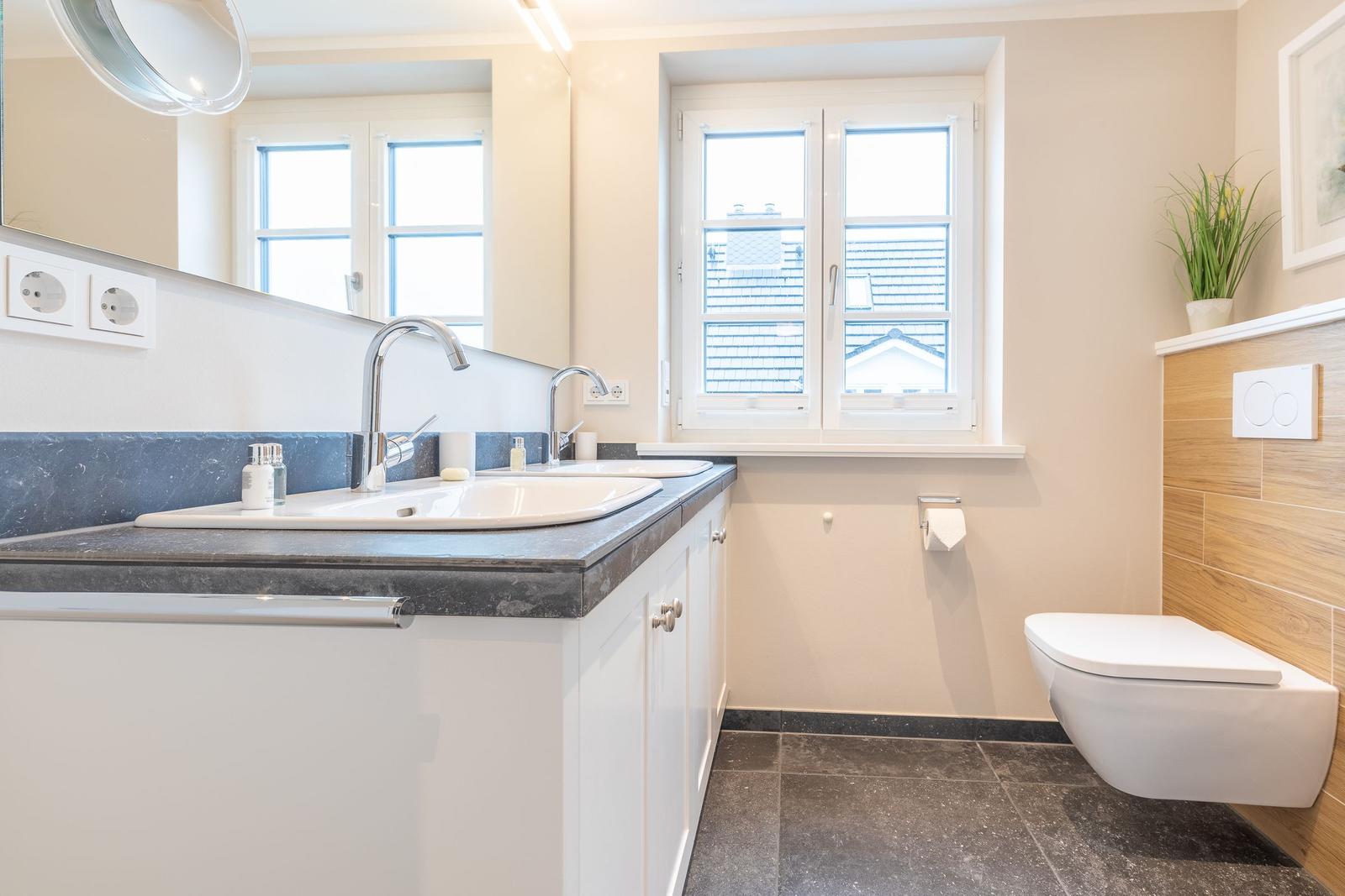 Bathroom with sink, mirror, and toilet. Window with view of rooftops.