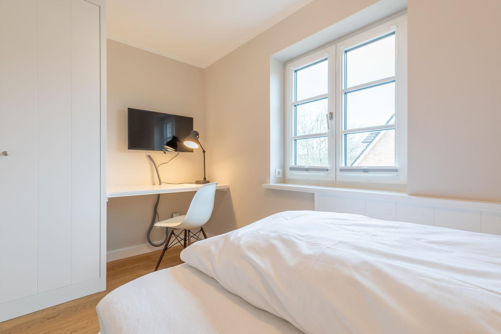 Bedroom with bed, desk, TV, and window.
