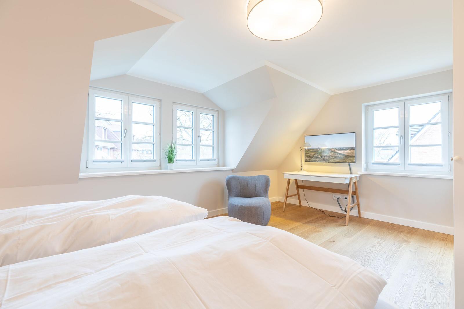 Room with two beds, desk, and windows.