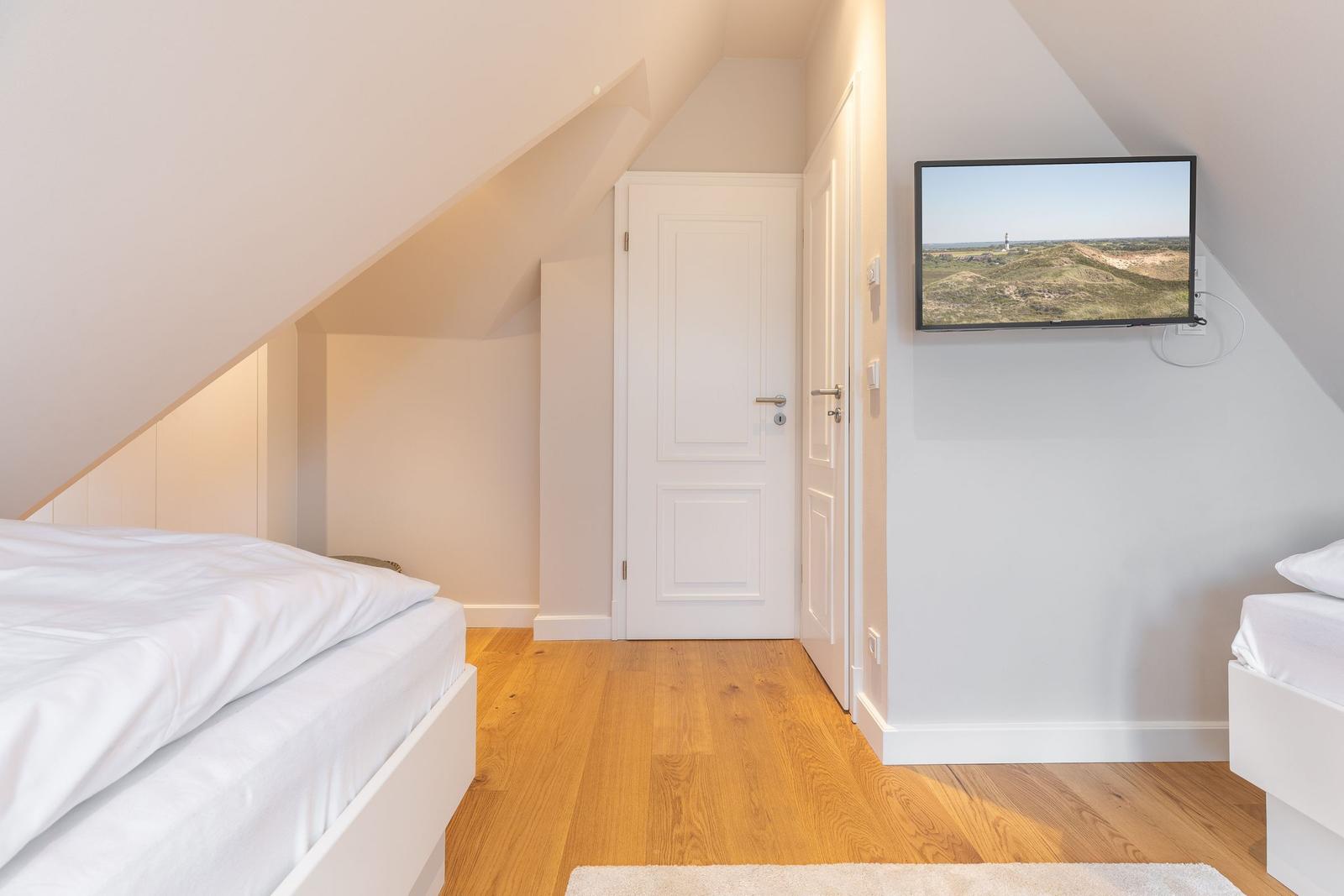 Room with two beds, wooden floor, and TV mounted on the wall.