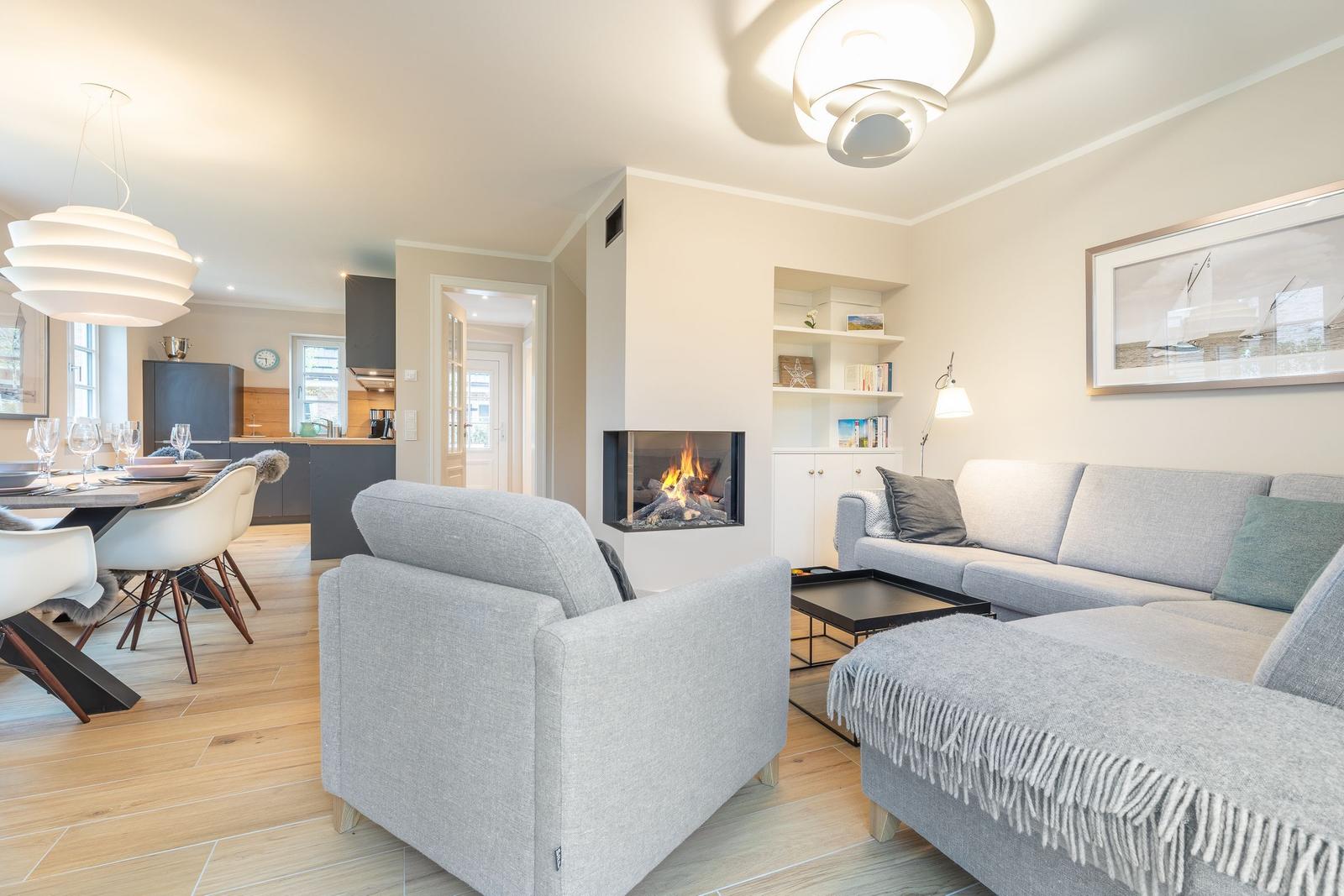Living room with fireplace, sofa, and dining table. Kitchen in background.