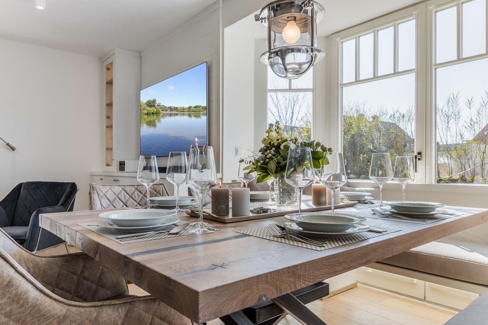 Esszimmer mit Holztisch, Stühlen und Fensterblick auf Wasser.