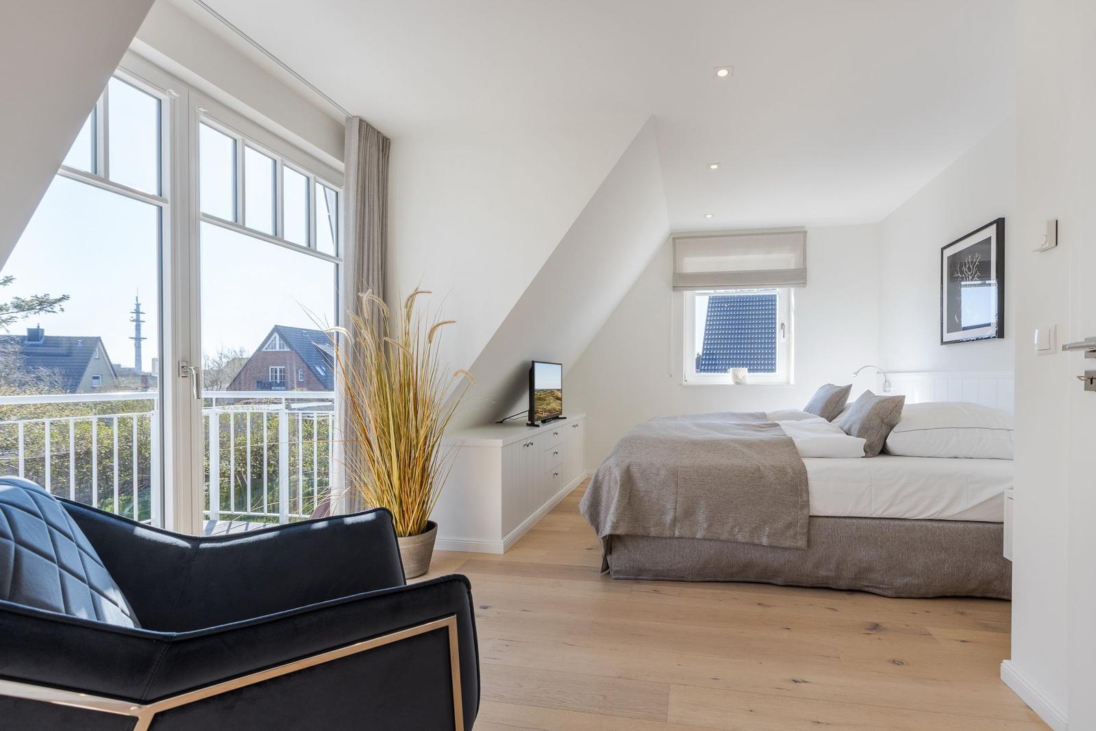 Schlafzimmer mit Dachschrägen, Balkon und Bett mit grauer Bettwäsche.