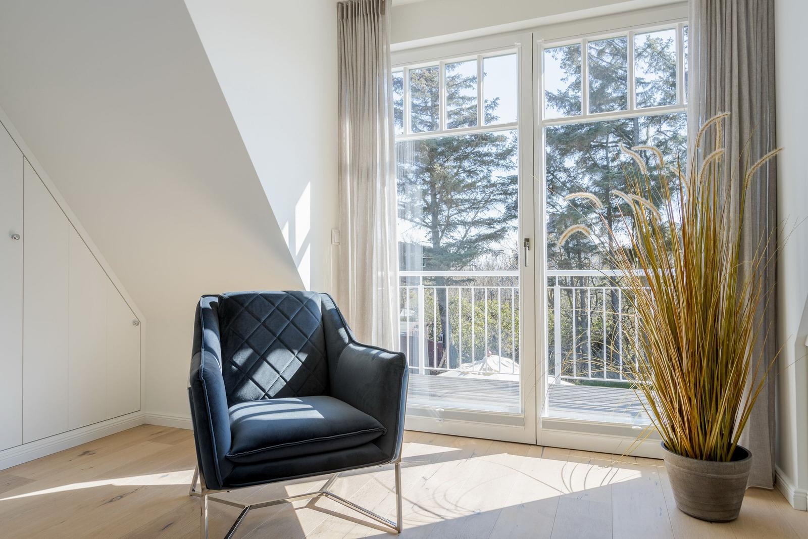Ein dunkler Sessel steht vor einer Glastür mit Blick auf Balkon und Bäume.