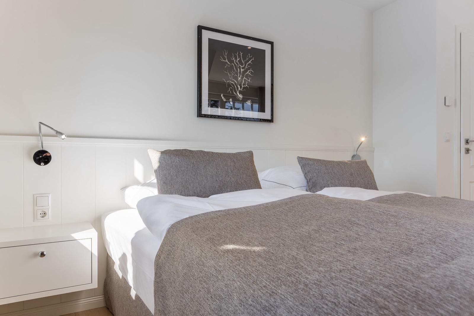 Doppelbett mit grauer Bettdecke und zwei Kissen. An der Wand hängt ein gerahmtes Bild.