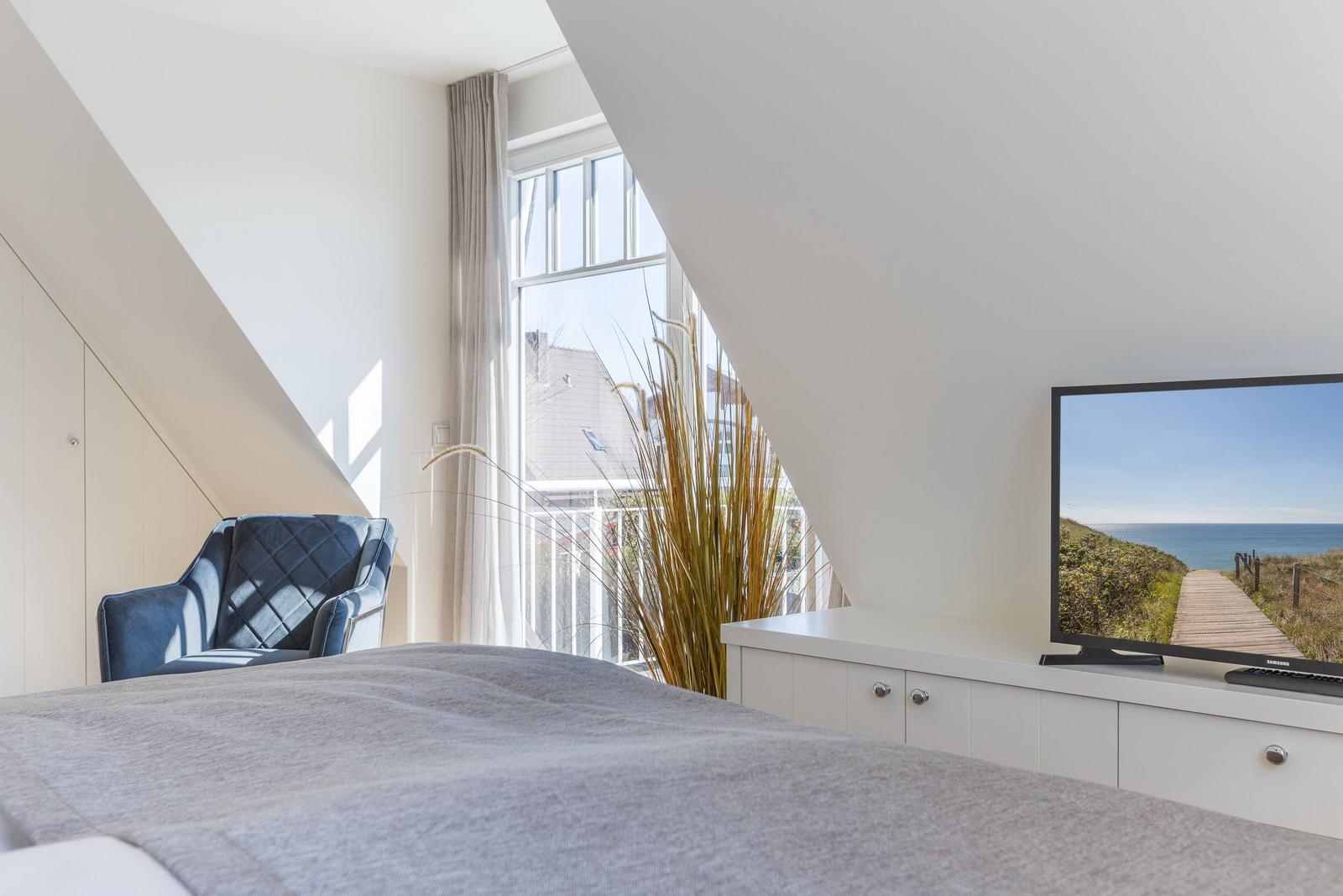 Schlafzimmer mit Blick auf Balkon und Meer. TV, Bett und Sessel sichtbar.