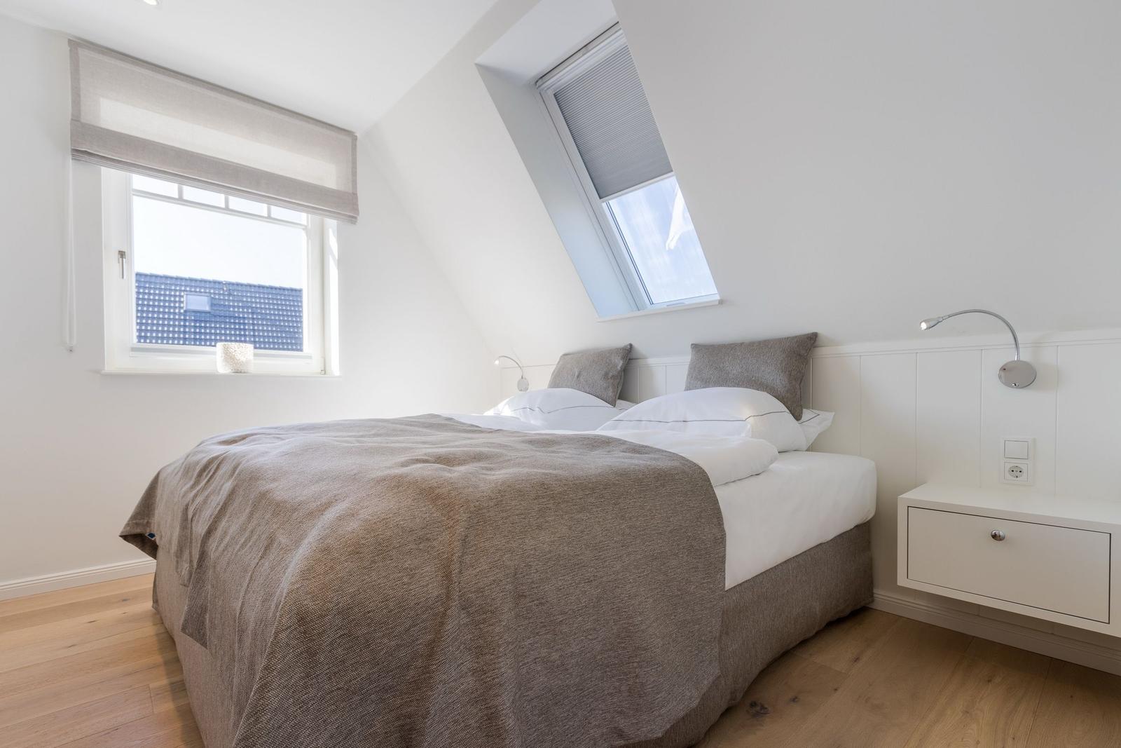 Schlafzimmer mit Dachschrägen, Bett, Nachttisch und Fenstern.