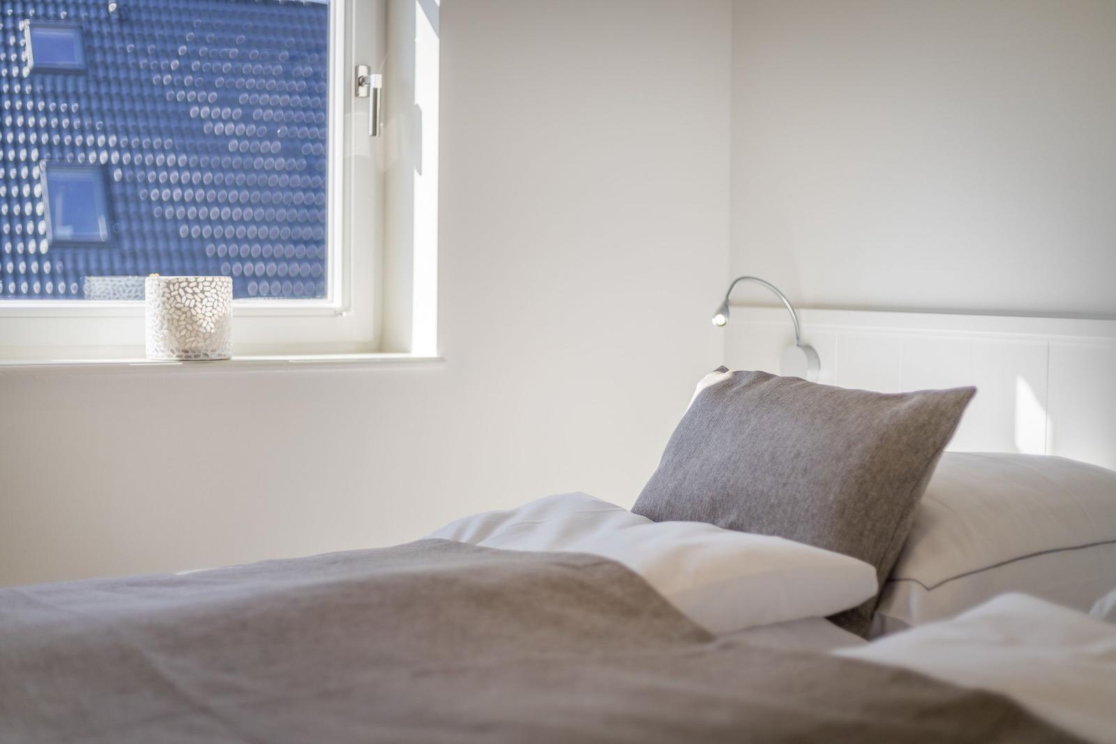 Schlafzimmer mit Bett, Kopfkissen und Fenster mit dekorativer Lampe.