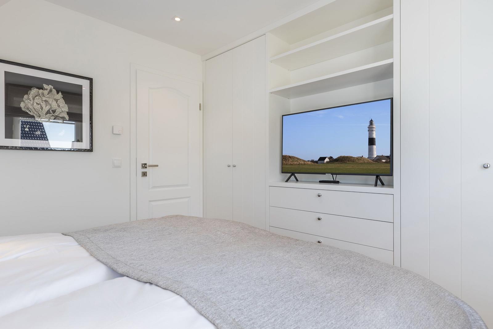 Schlafzimmer mit Bett, TV und weißen Schränken.