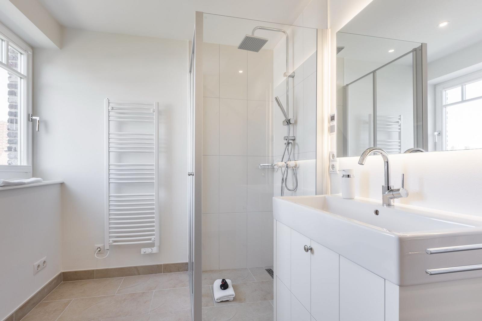 Badezimmer mit Dusche, Waschbecken und Heizkörper.