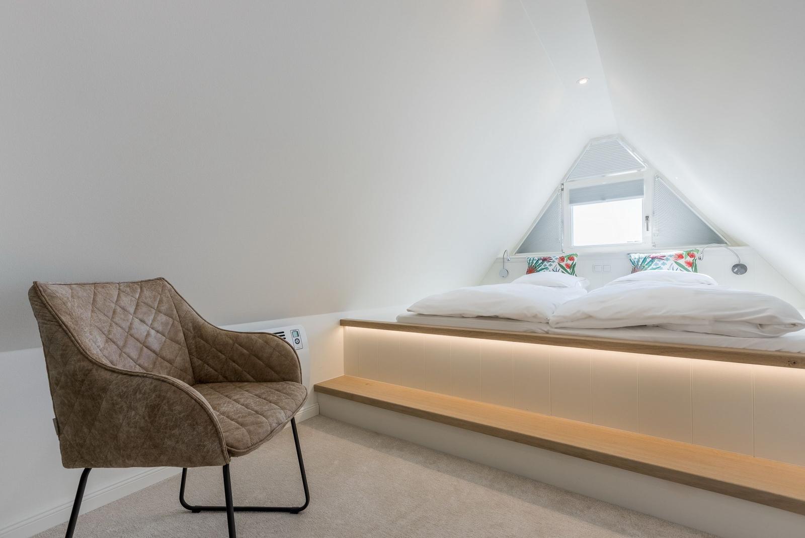 Schlafzimmer mit Dachschräge, Bett mit Holzrahmen und Sitzbank. Braune Ledermöbel.