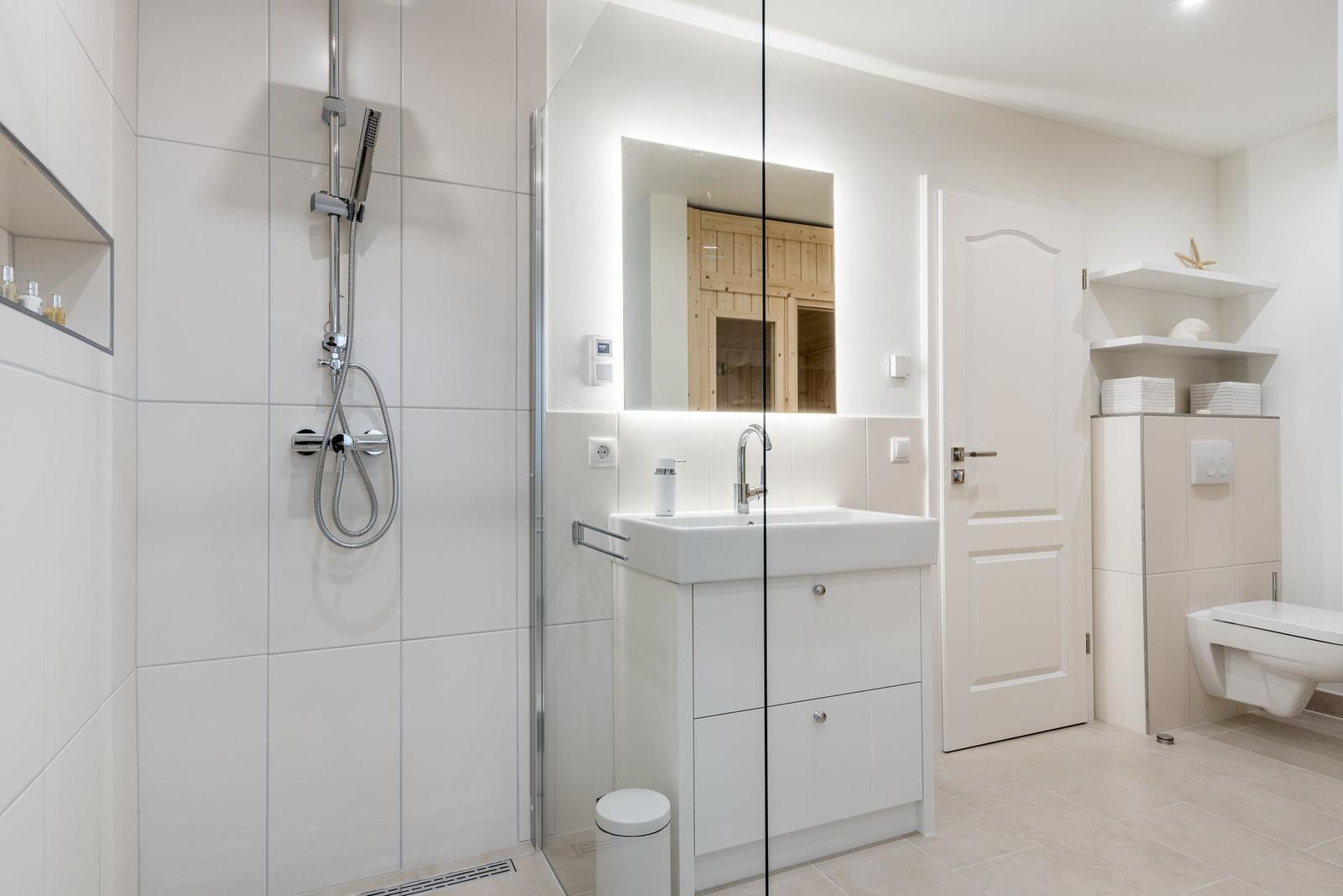 Badezimmer mit Dusche, Waschbecken und Toilette. Spiegelschrank und Holzverkleidung sichtbar.