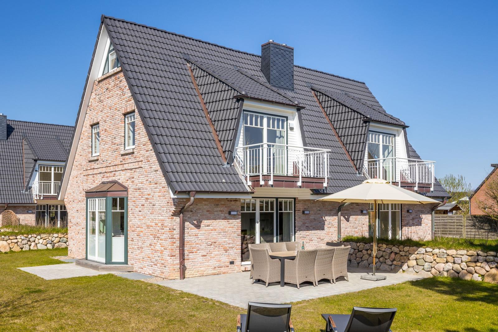 Haus mit Steinmauer, Terrasse und Gartenbereich mit Sitzgruppe.