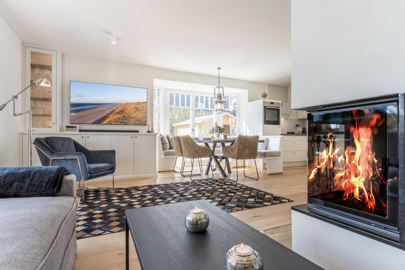 Wohn- und Essbereich mit Kamin, TV und Essplatz. Holzboden und modernes Mobiliar.