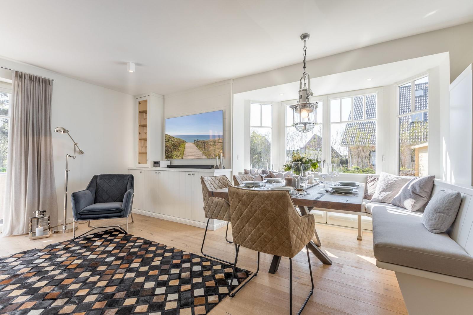 Wohn- und Essbereich mit Esszimmertisch, Sitzbank und Fernseher an der Wand.