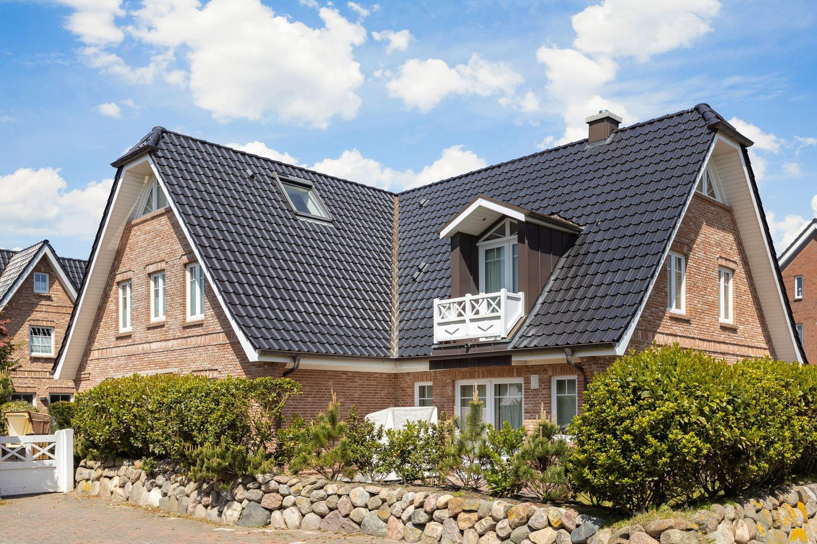 A two-story house with brick facade and dark roof. A well-kept garden is in front of the house.