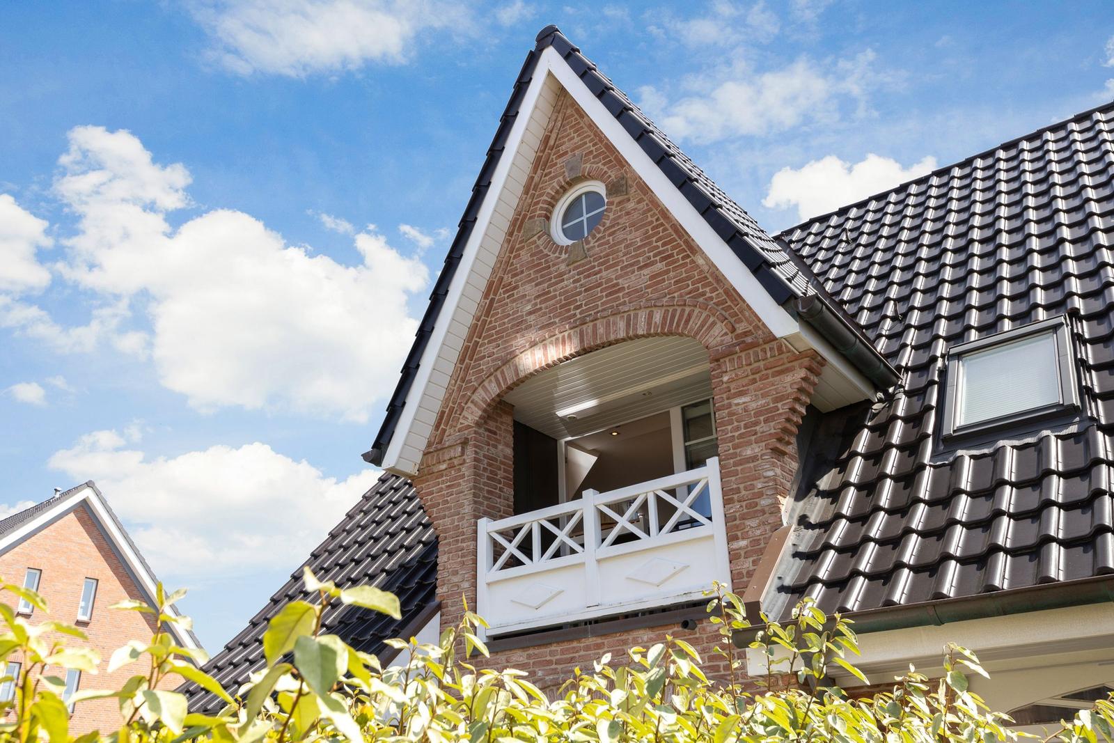 Two-story house with balcony and tiled roof under blue sky.