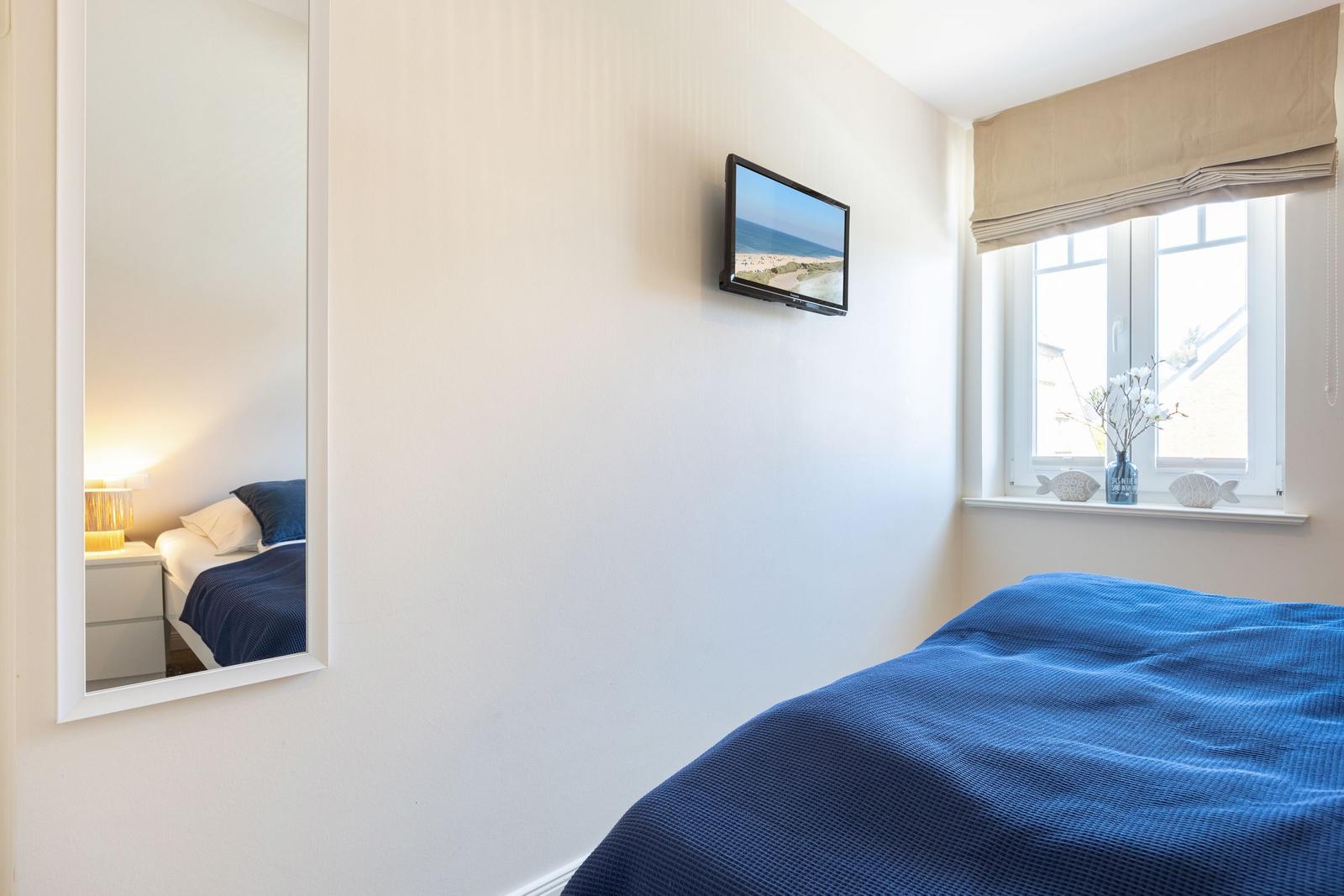 Bedroom with blue bedding, wall-mounted TV, and window with view.