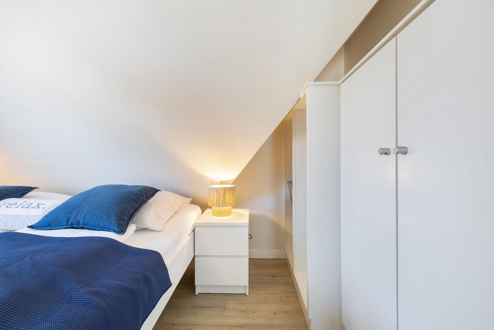 Bedroom with bed, nightstand, and wardrobe under sloped ceiling.