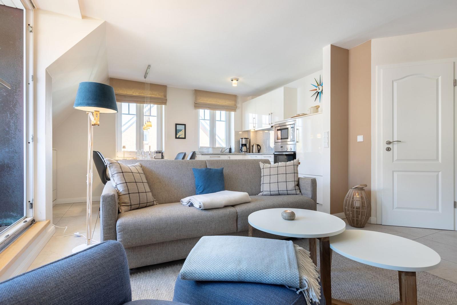 Living and kitchen area with sofa, tables, and windows.