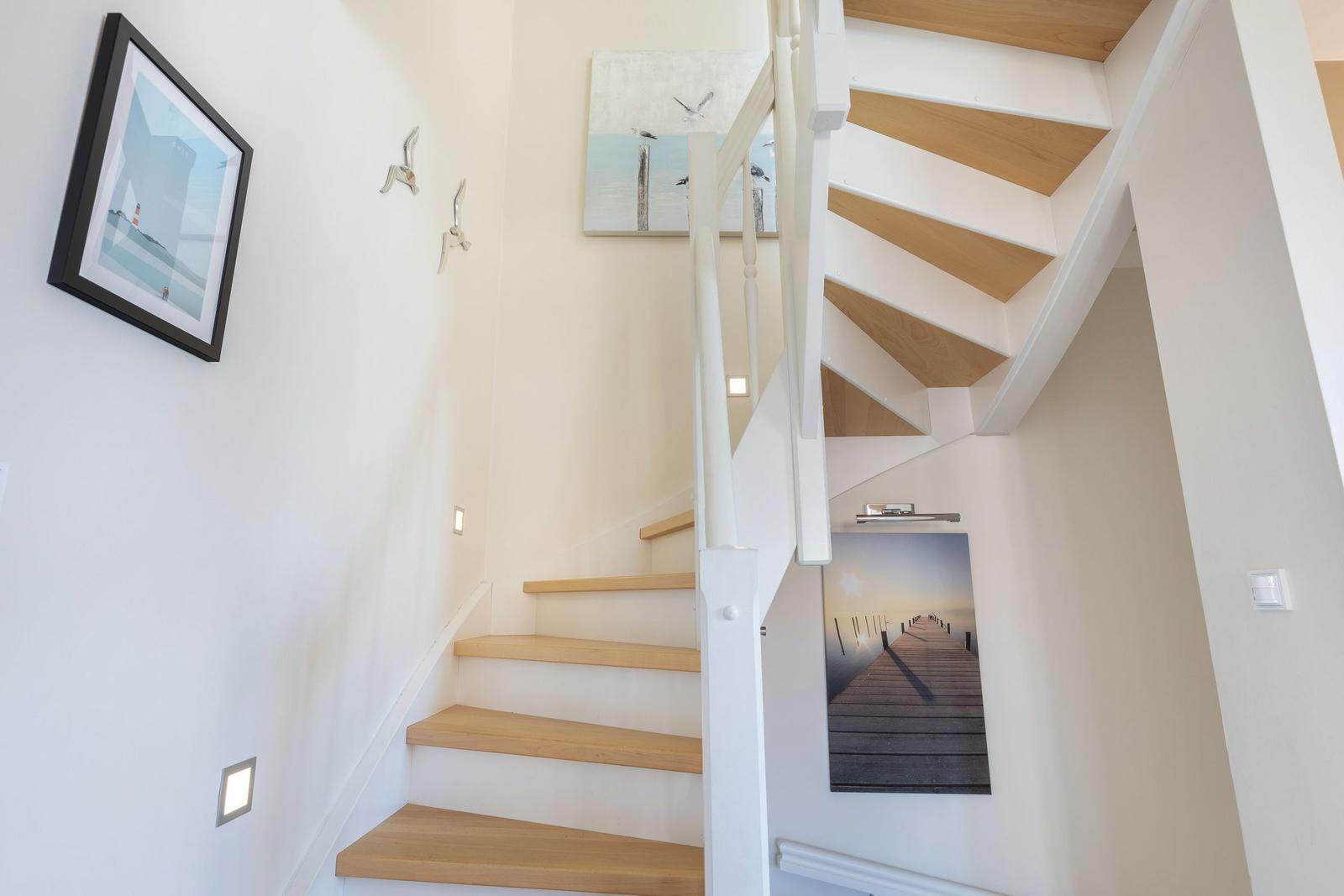 Light staircase with wooden steps and white railings. Wall pictures show pier and sea.