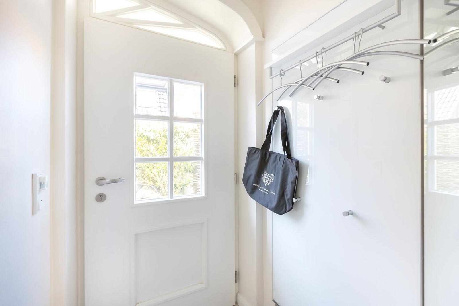 Bright entrance hall with white door and coat rack. A bag hangs on a hook.