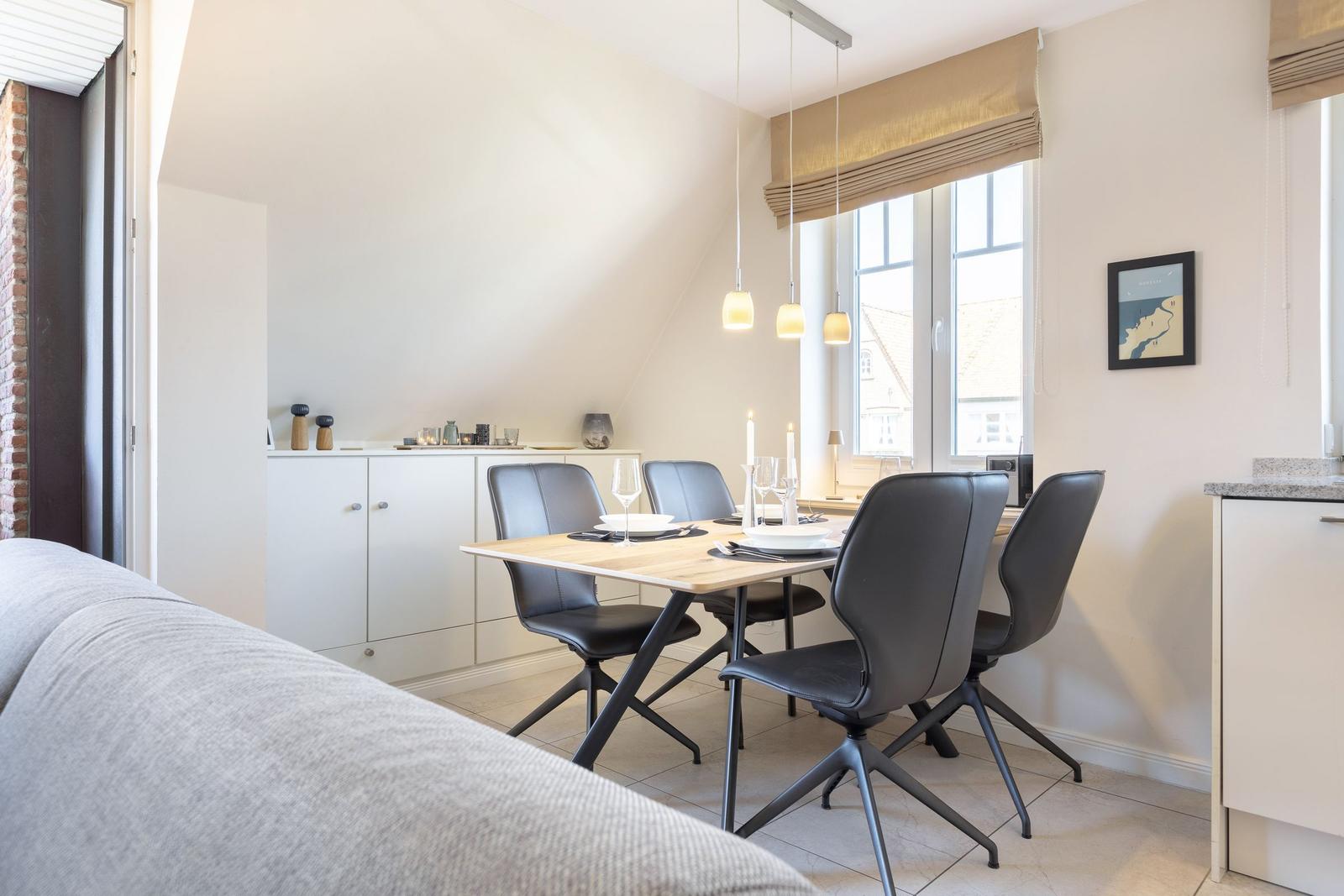 Dining area with table, chairs, and window. Background: white cabinets and pendant lights.