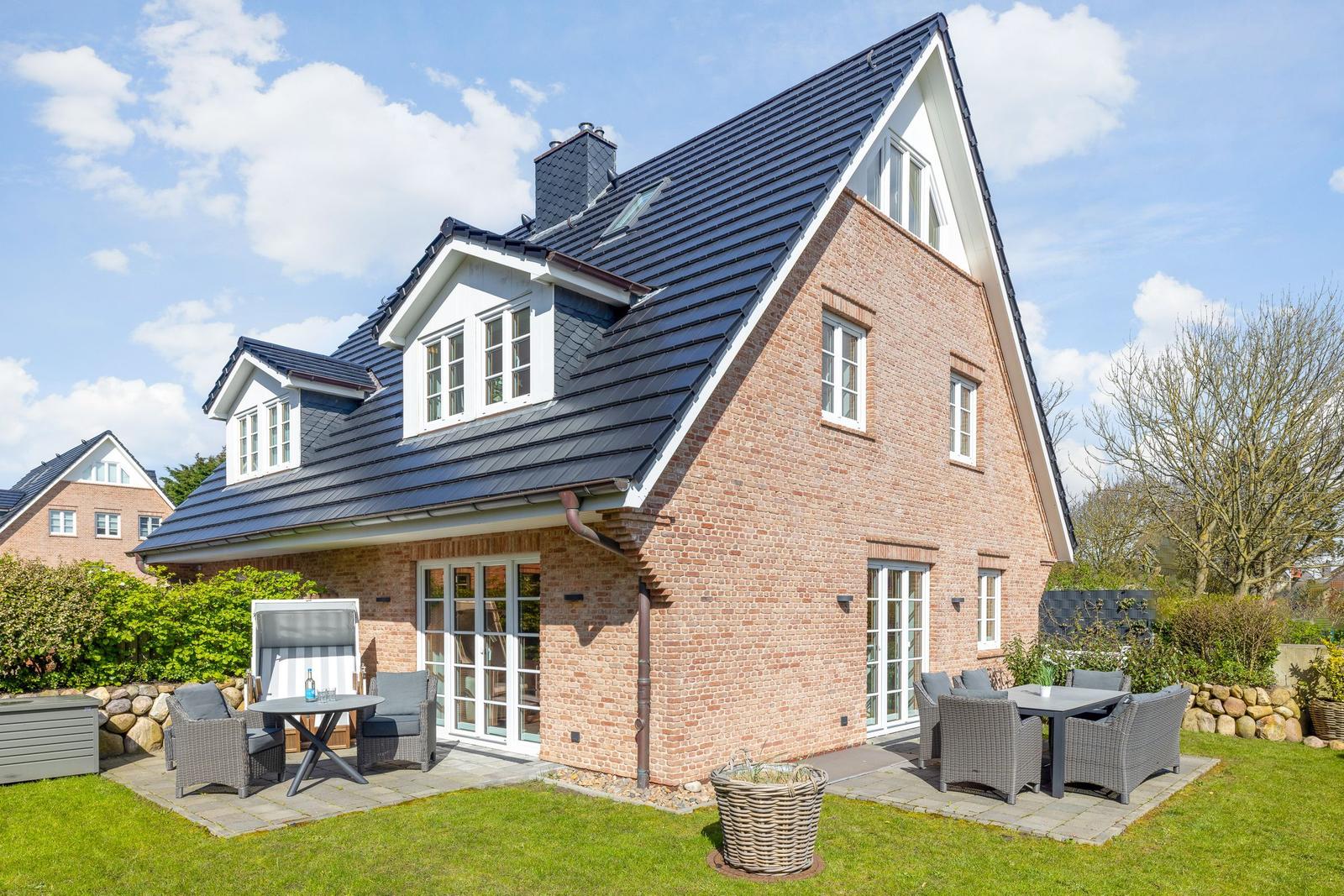 Ein zweistöckiges Haus mit rotem Backstein und dunklem Dach. Außenbereich mit Gartenmöbeln.