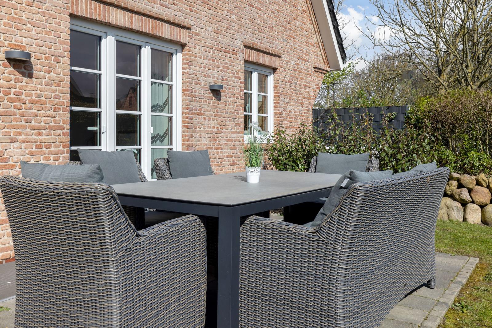 Terrasse mit Sitzgruppe vor Backsteinhaus mit Fenstern.